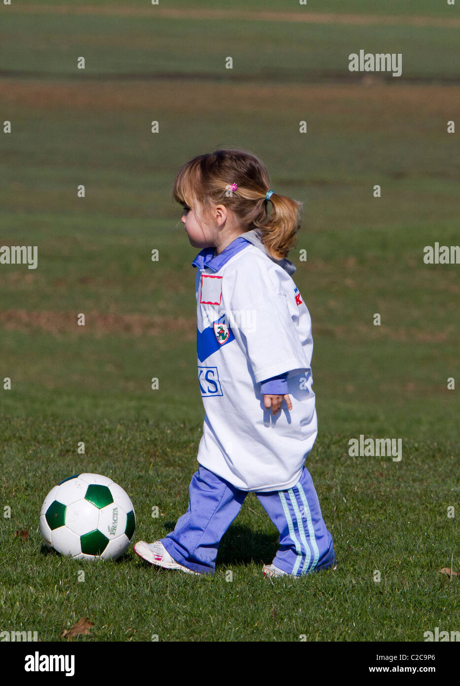 Una pequeña niña jugando pateando una pelota de fútbol Fotografía de ...