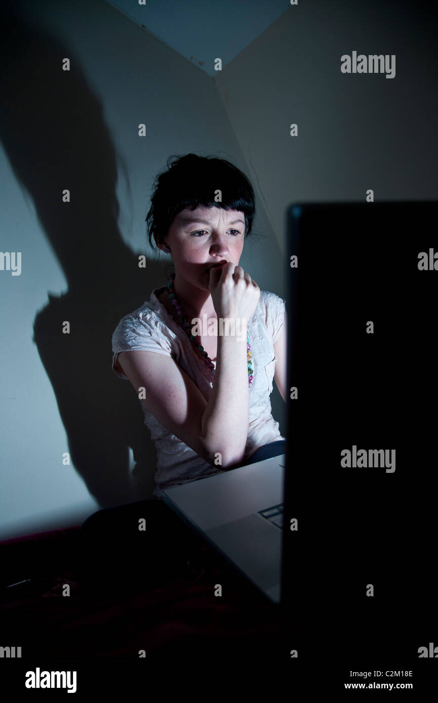 Una joven estudiante universitaria en el Reino Unido trabajan en equipo portátil en su dormitorio en casa preocupados por virus de correo facebook bug Foto de stock