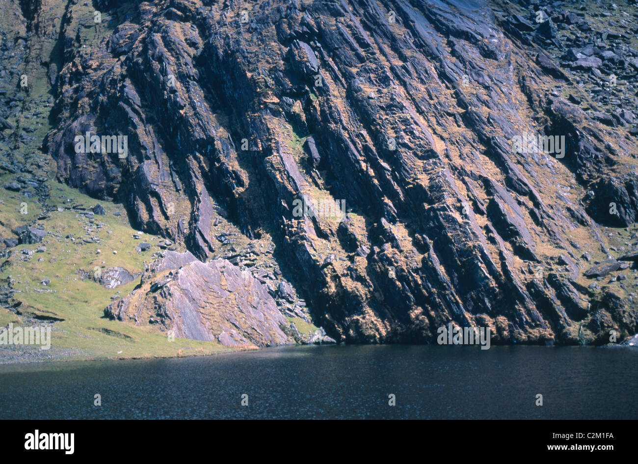 Roca arenisca plegada junto a un lago en la montaña, Knockmoyle Coomavoher, Condado de Kerry, Irlanda. Foto de stock