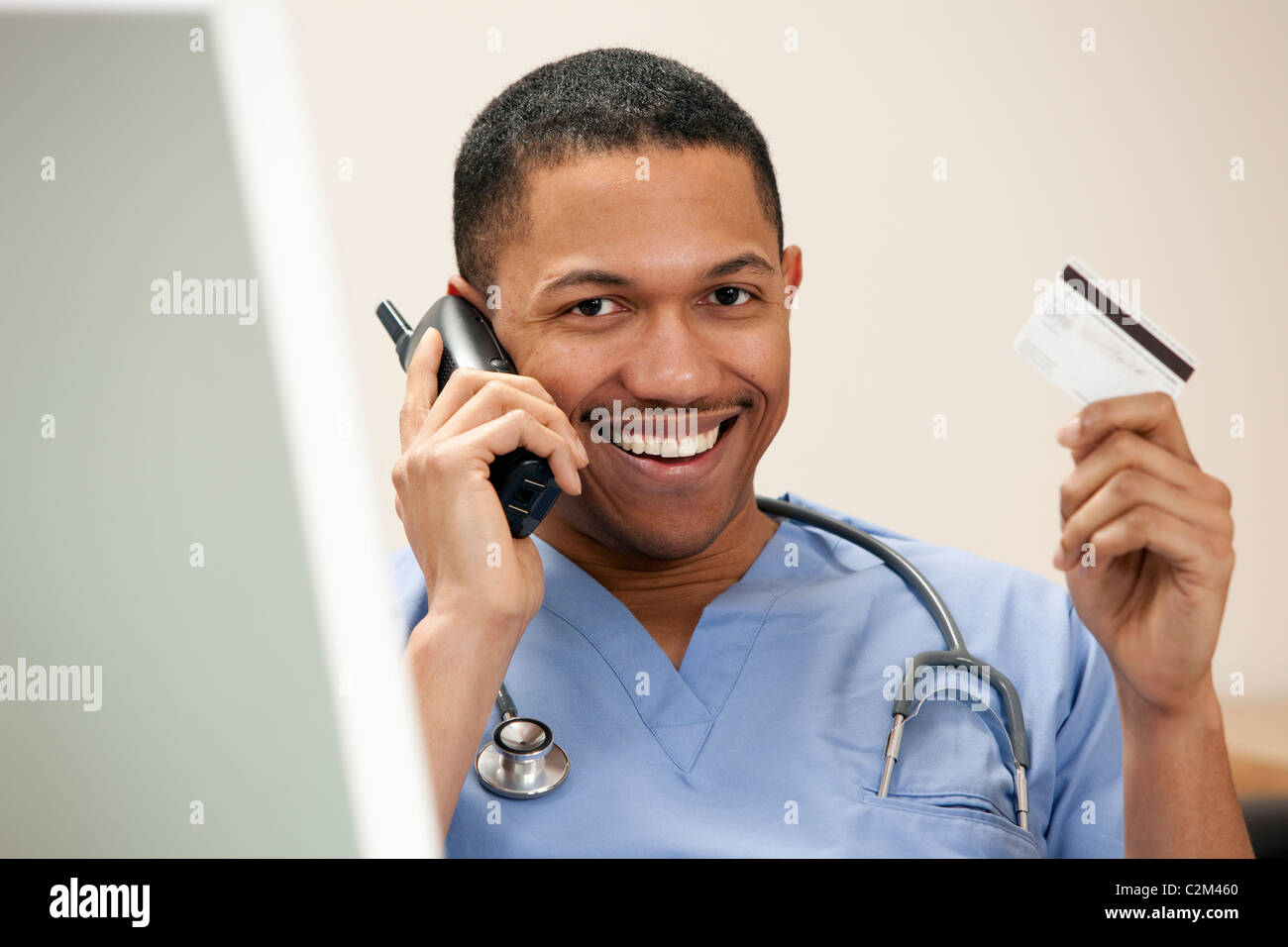 Doctor americano africano en el teléfono sentado en el equipo con su tarjeta de crédito Foto de stock