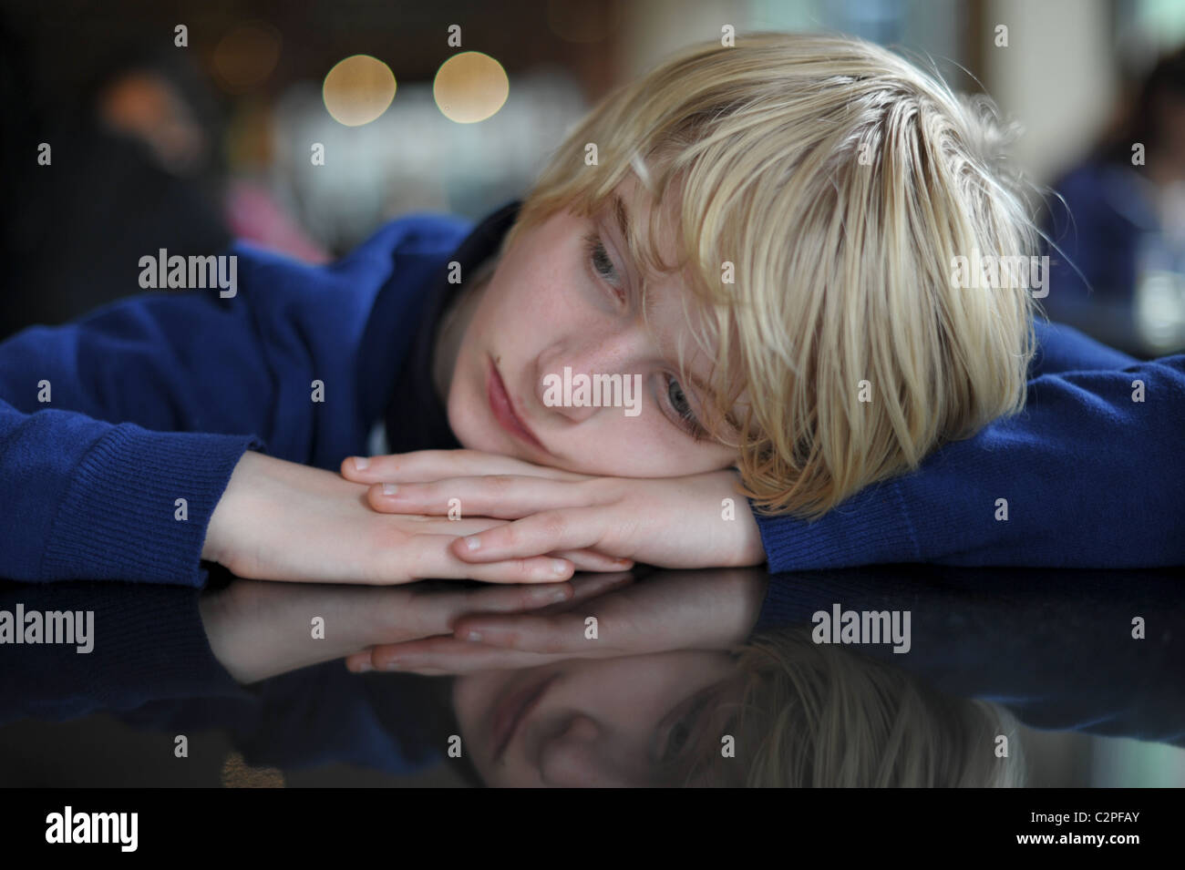 Rubio adolescente descansando su cabeza en sus manos en un restaurante mirando aburrido y triste Foto de stock