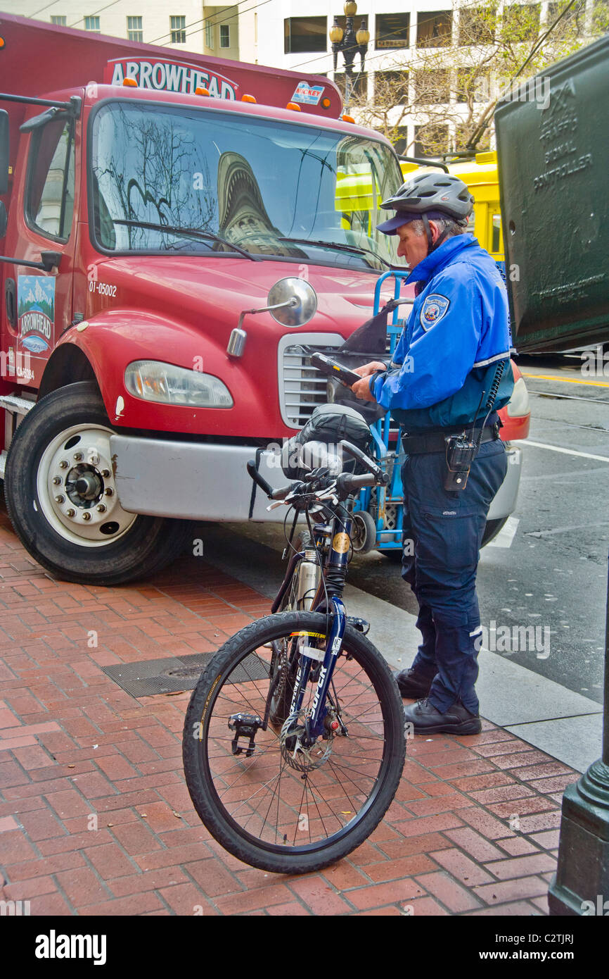 Utilizando un equipo inalámbrico, una bicicleta de la policía montada del alcaide de estacionamiento escribe una violación billete para un camión estacionado ilegalmente. Foto de stock