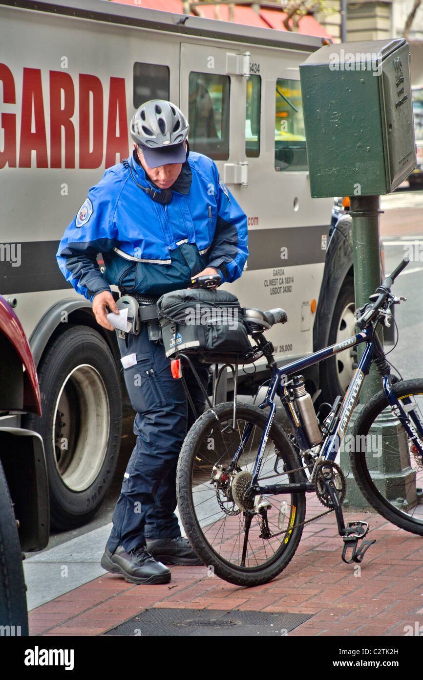 Utilizando un equipo inalámbrico, una bicicleta de la policía montada del alcaide de estacionamiento escribe una violación billete para un camión estacionado ilegalmente. Foto de stock