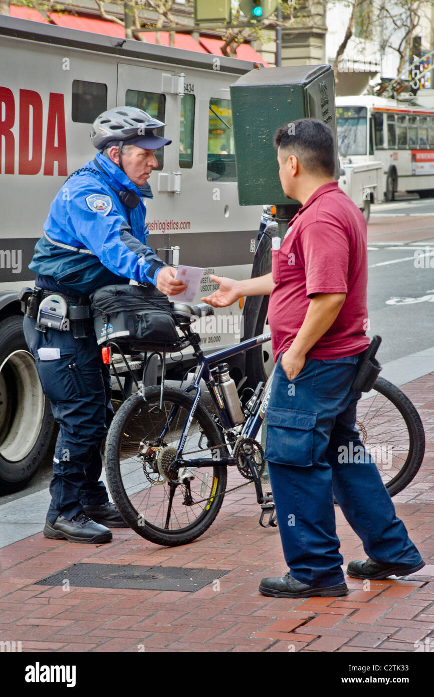 Una bicicleta de la policía montada del alcaide de aparcamiento da una violación billete al conductor de un camión estacionado ilegalmente en San Francisco, CA. Foto de stock