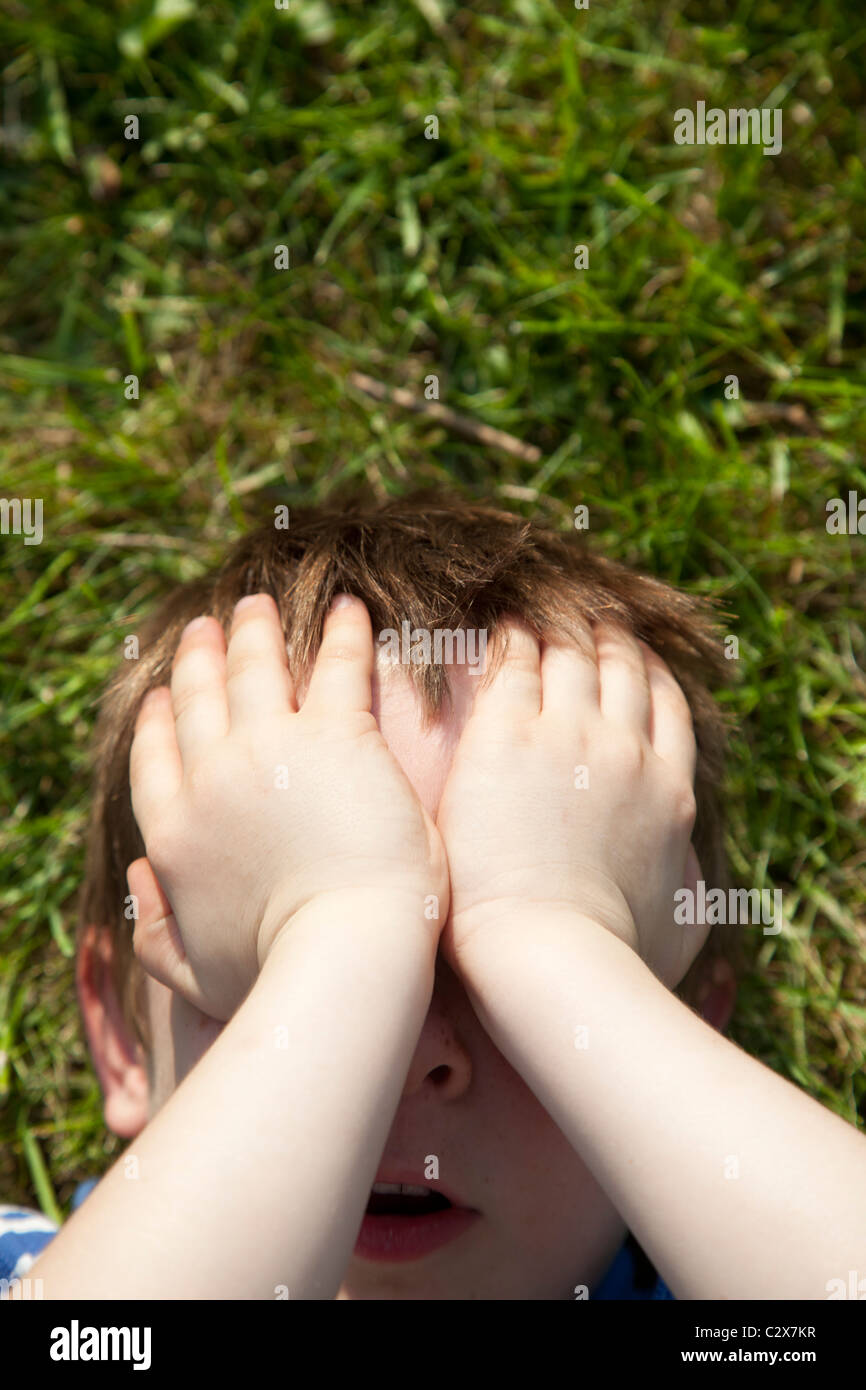 Un joven cubre sus ojos en jugar con sus manos. Foto de stock