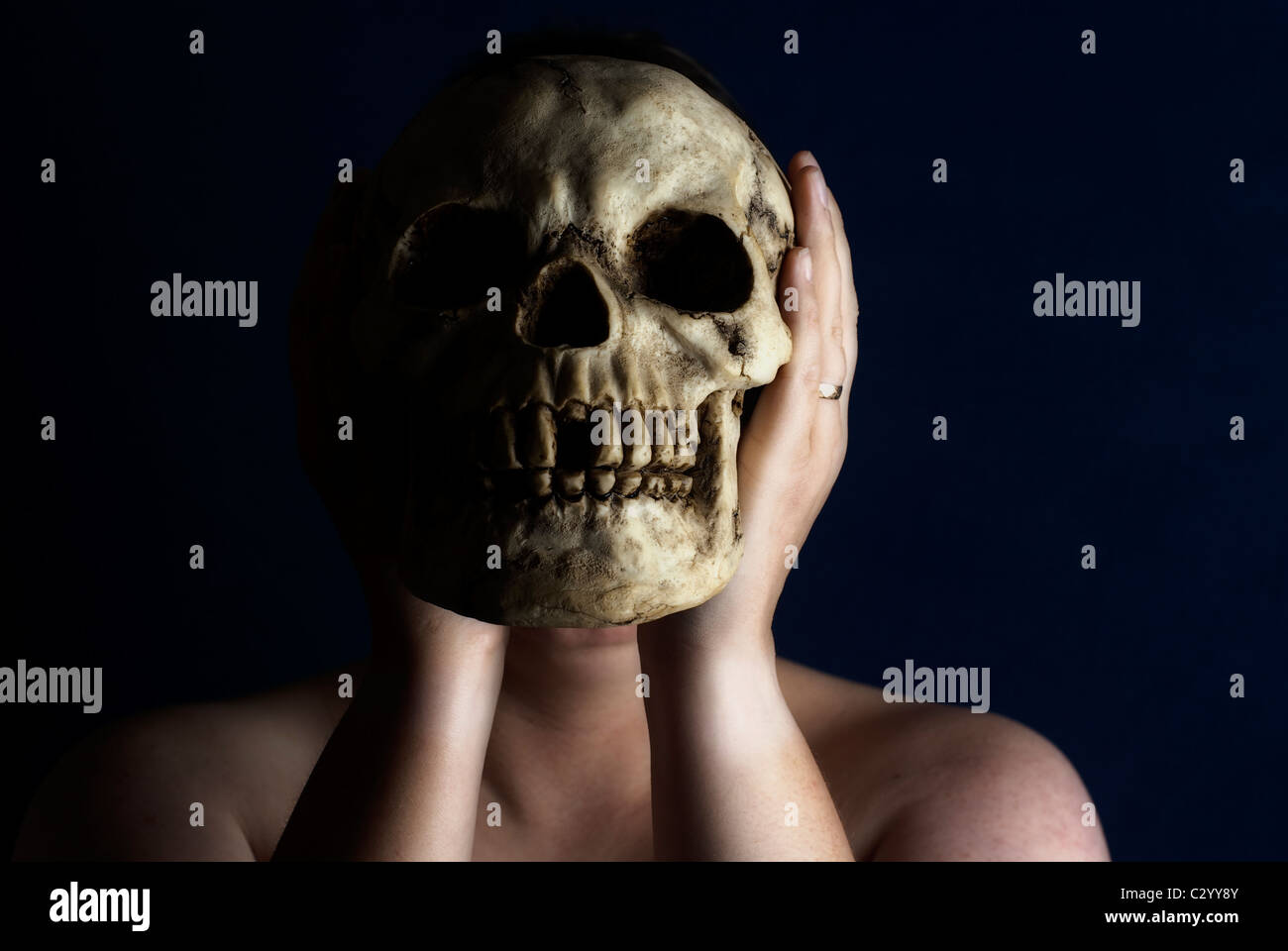 Una mujer sostiene un cráneo humano delante de su cara contra un fondo negro. Foto de stock