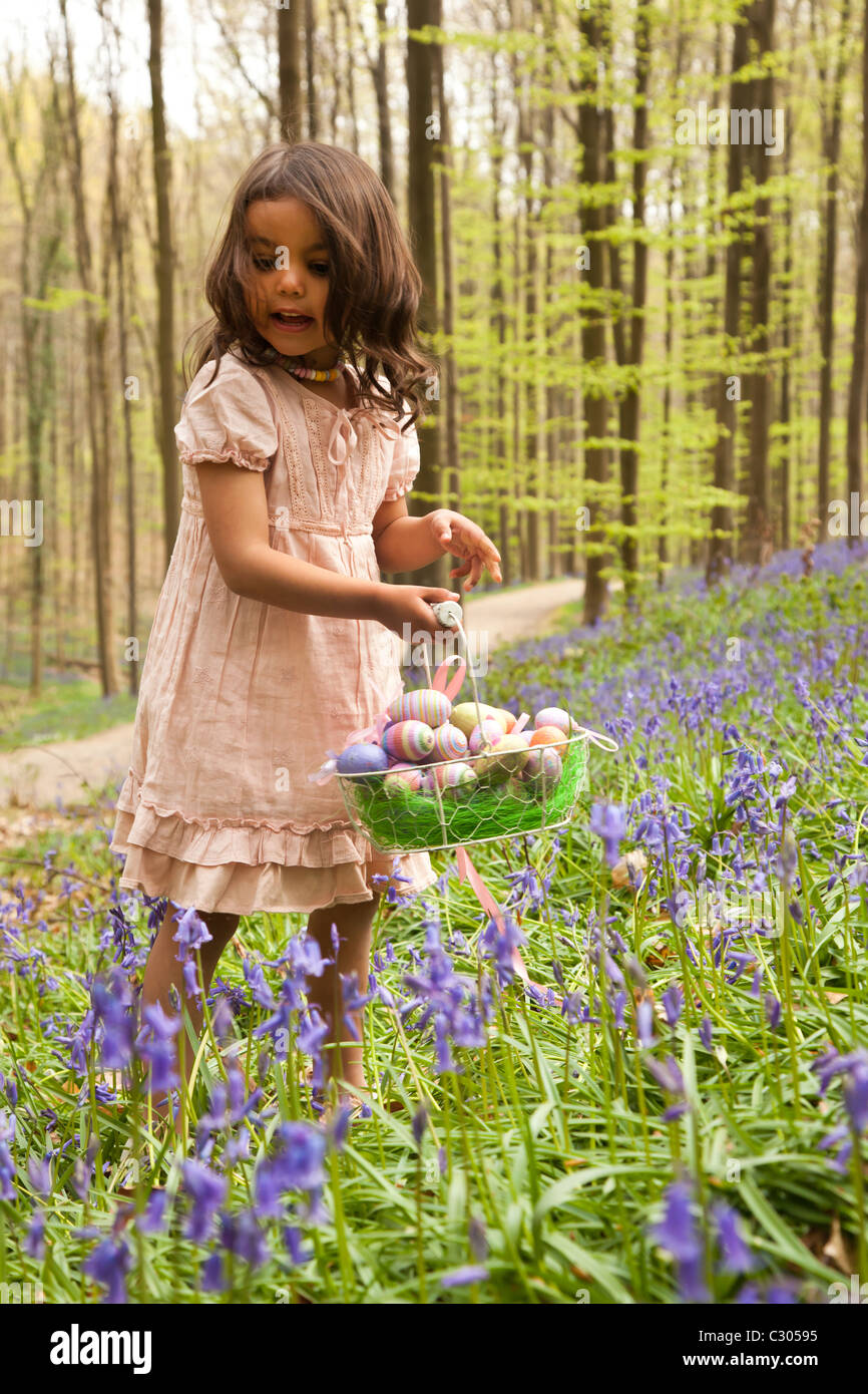 Little girl looking for de huevos de Pascua, en el bosque entre campanillas Foto de stock