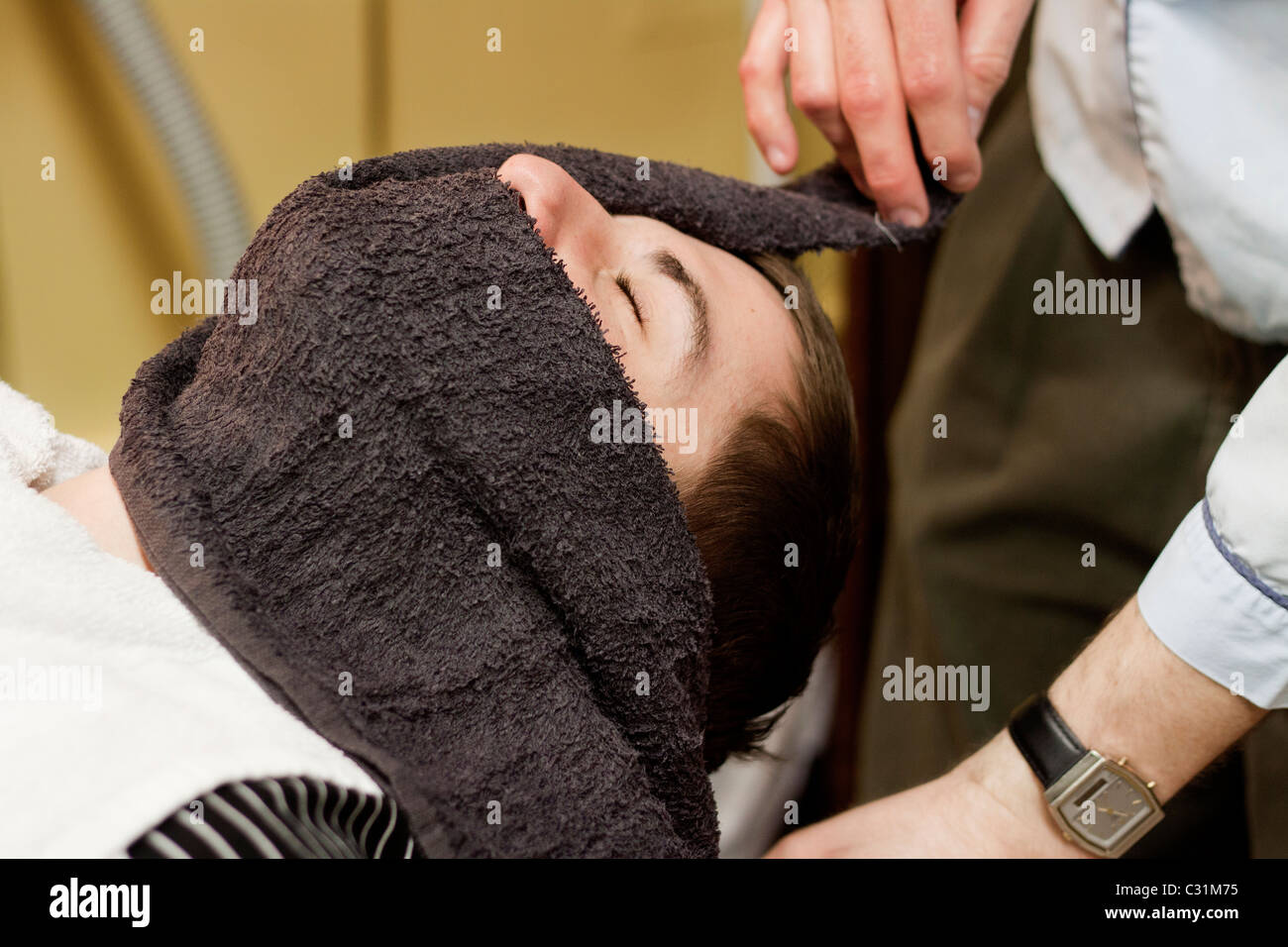 Un hombre obtiene una toalla caliente sobre su rostro antes de afeitar navaja recta en Omaha, Nebraska, EEUU. Foto de stock