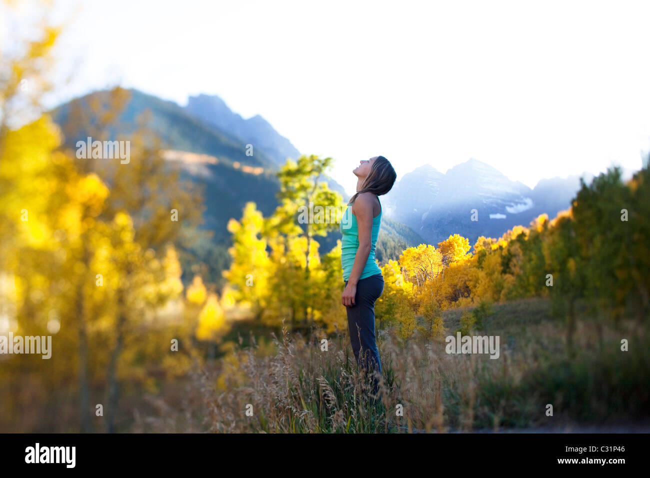 Una joven mujer respira profundamente rodeado por bosques de oro y picos nevados. Foto de stock