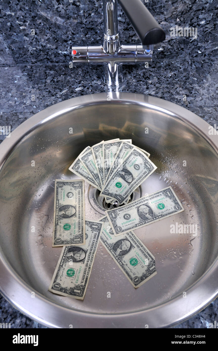 Dólares estadounidenses en un fregadero con agua de drenaje concepto buen dinero vaya por el desagüe. Foto de stock