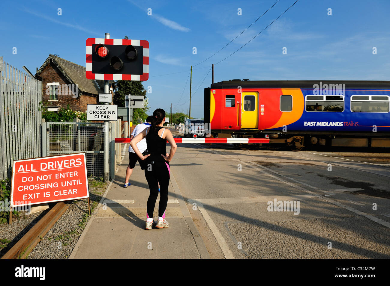 Corredores esperando en un paso a nivel, mientras que un tren de cercanías pasa Beeston Nottingham, Inglaterra Foto de stock