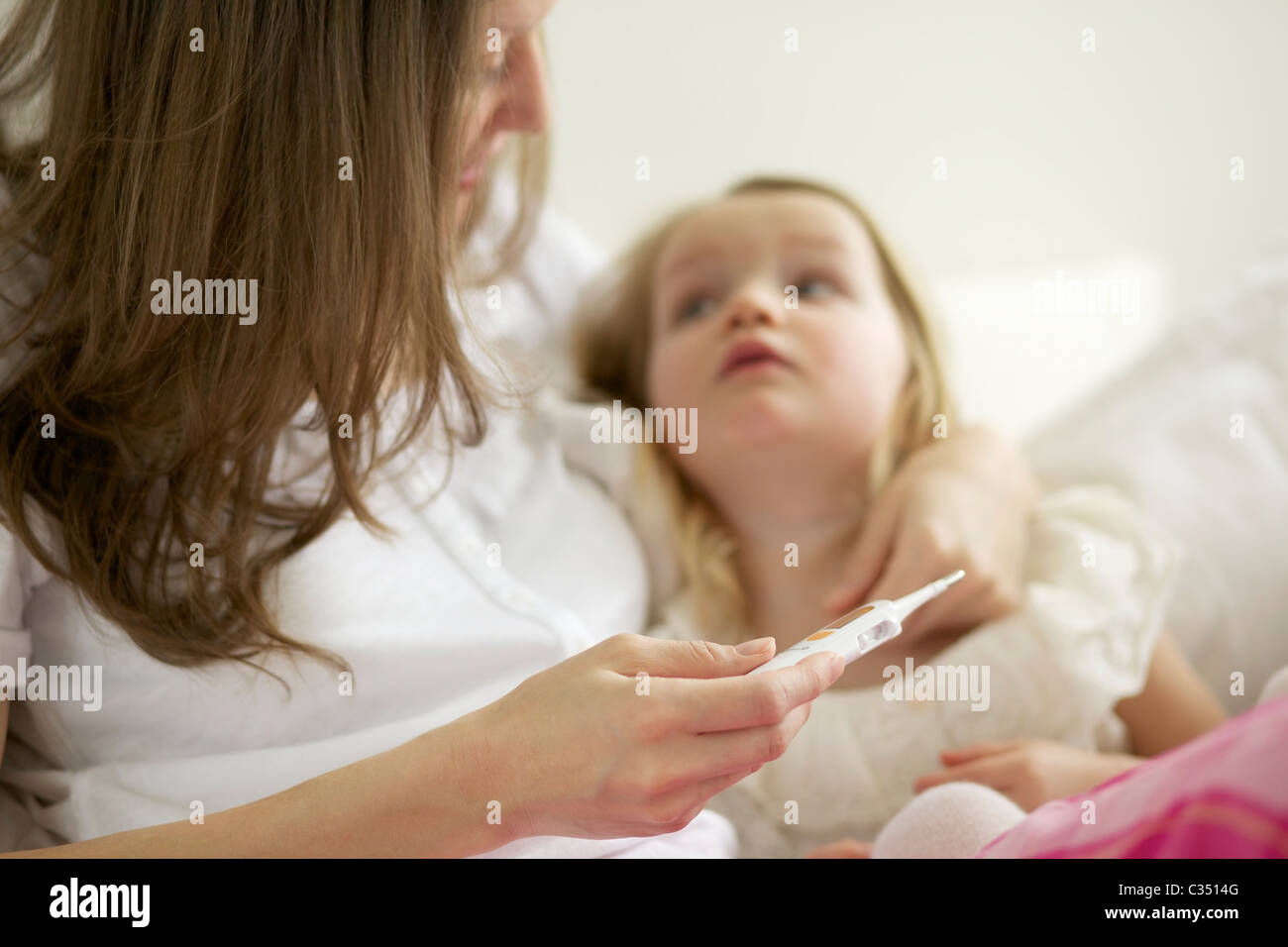 Comprobación de la madre a su hija la fiebre con el termómetro digital Foto de stock