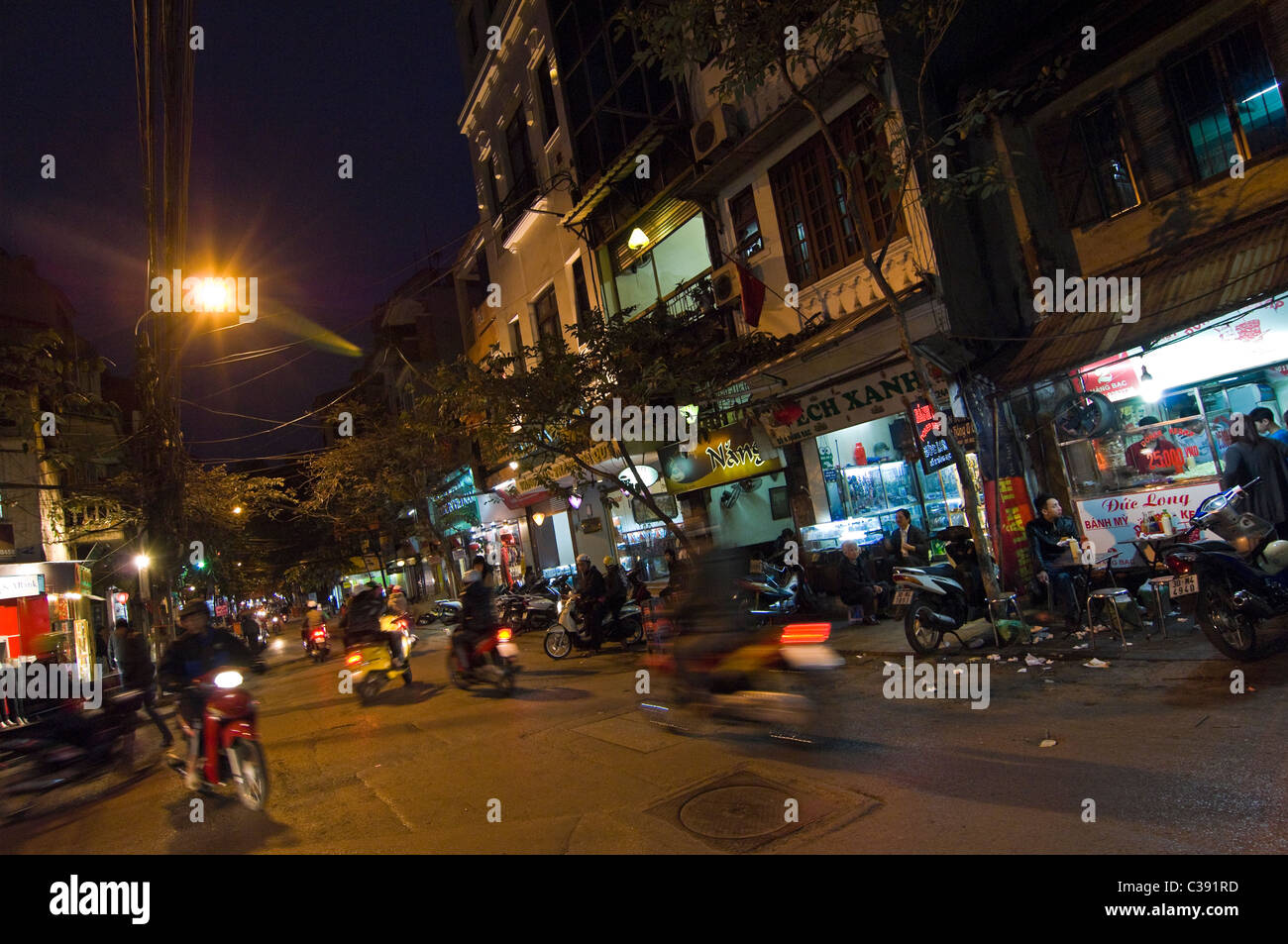 Vista nocturna de una horizontal streetscene típicas del barrio antiguo de Hanoi, con tiendas abiertas para los negocios y los ciclomotores pasando Foto de stock