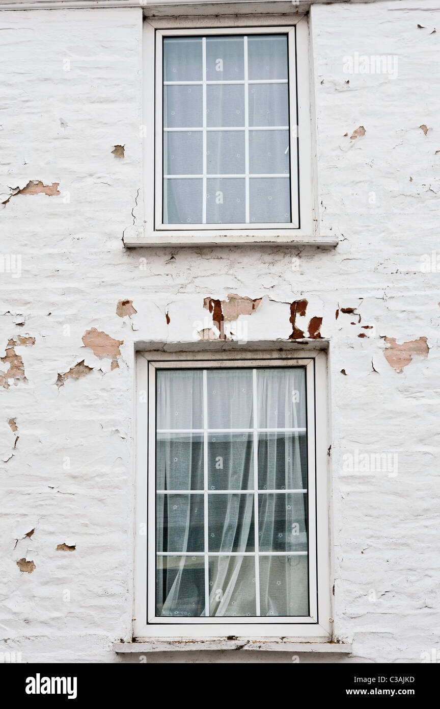 Dos ventanas en una pared pintada de blanco. La pintura está decayendo y  pelando la pared debido a la exposición al clima costero Fotografía de  stock - Alamy