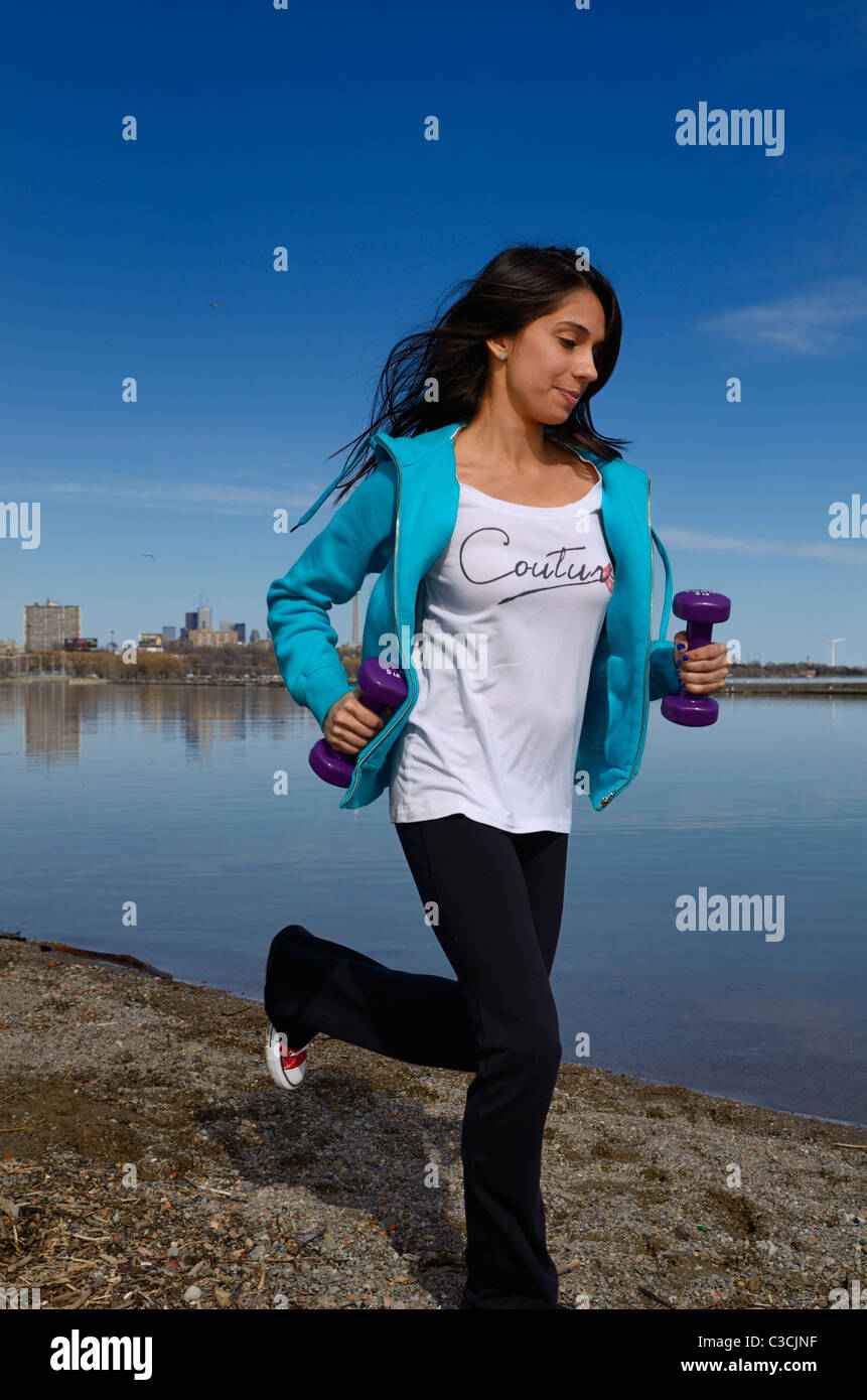 India oriental adolescente corriendo por la orilla del lago Ontario en Toronto con pesas de mano contra el cielo azul Foto de stock
