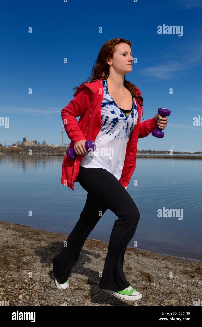 Adolescente corriendo por la orilla del lago Ontario en Toronto con pesas de mano contra el cielo azul Foto de stock