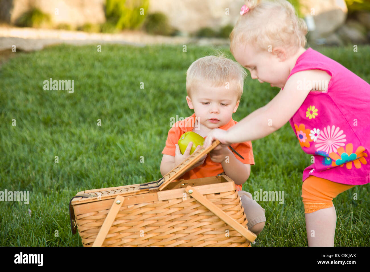 Hermano y hermana gemela lindos bebés jugando con Apple y cesta de picnic en el parque. Foto de stock