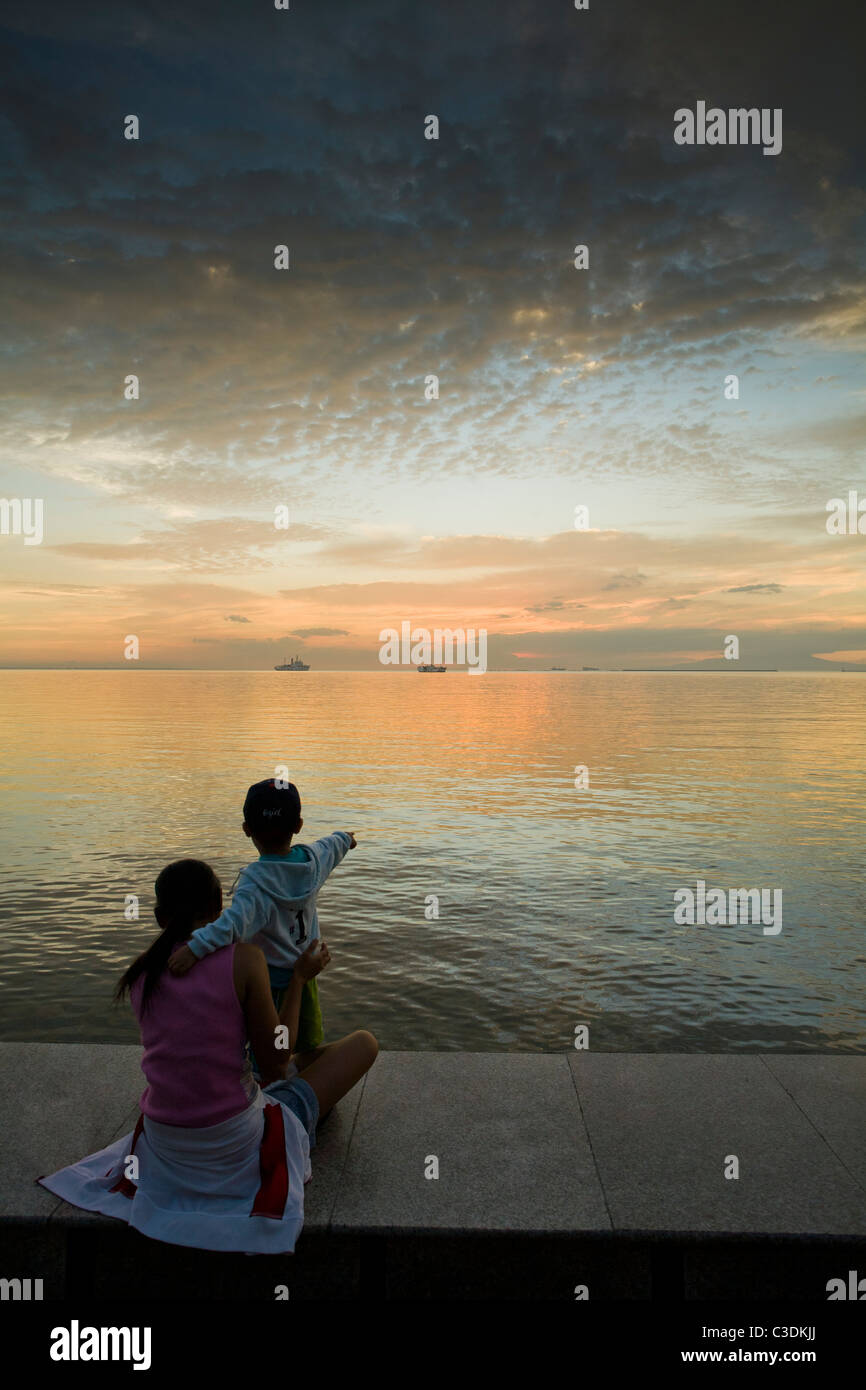 Un niño con su madre, señala el horizonte al atardecer sobre la bahía de Manila, Filipinas Foto de stock
