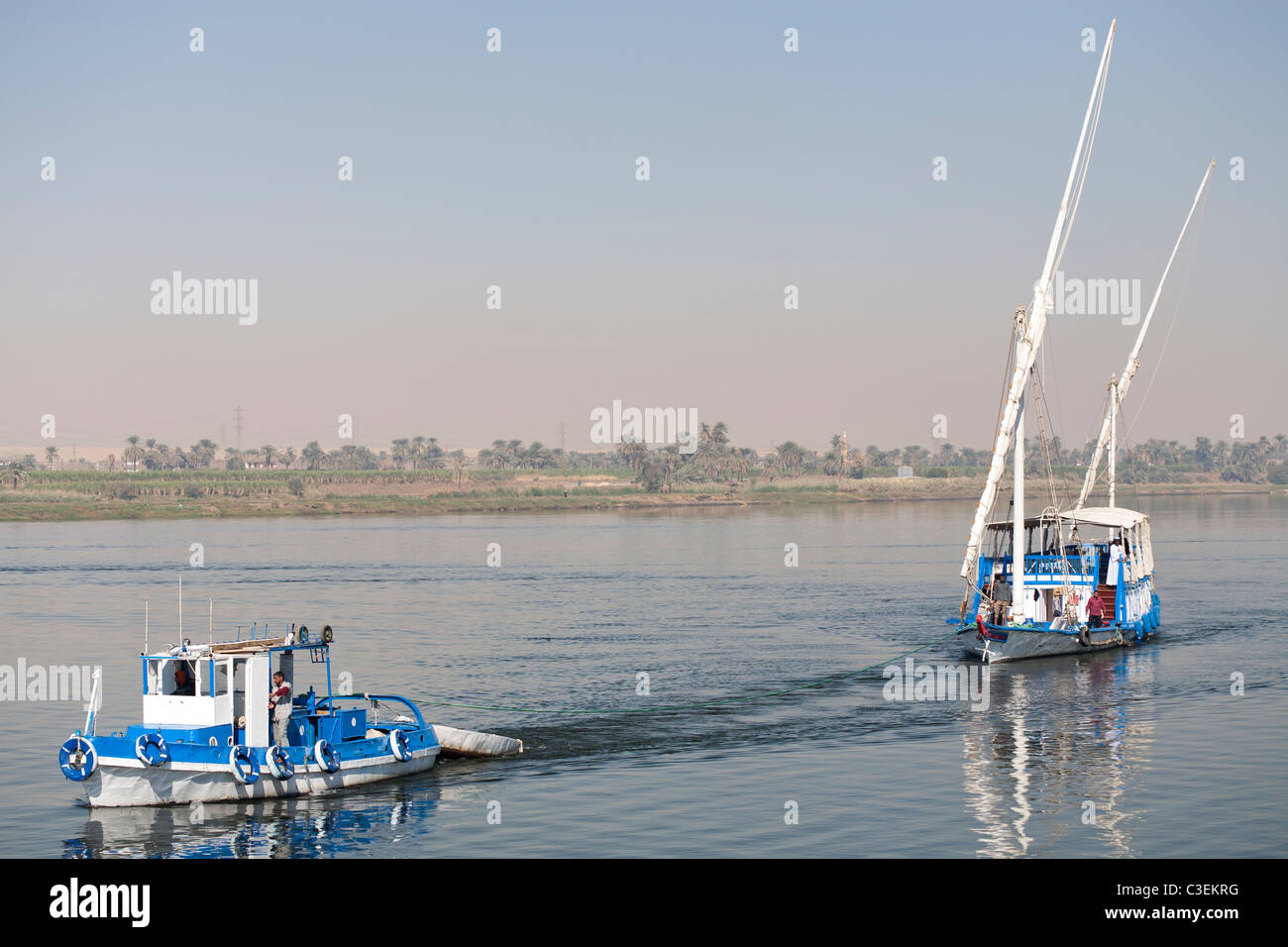 Una dahabiya siendo remolcado por embarcaciones pequeñas a sus amarras en las orillas del río Nilo en aguas tranquilas, Egipto, África Foto de stock