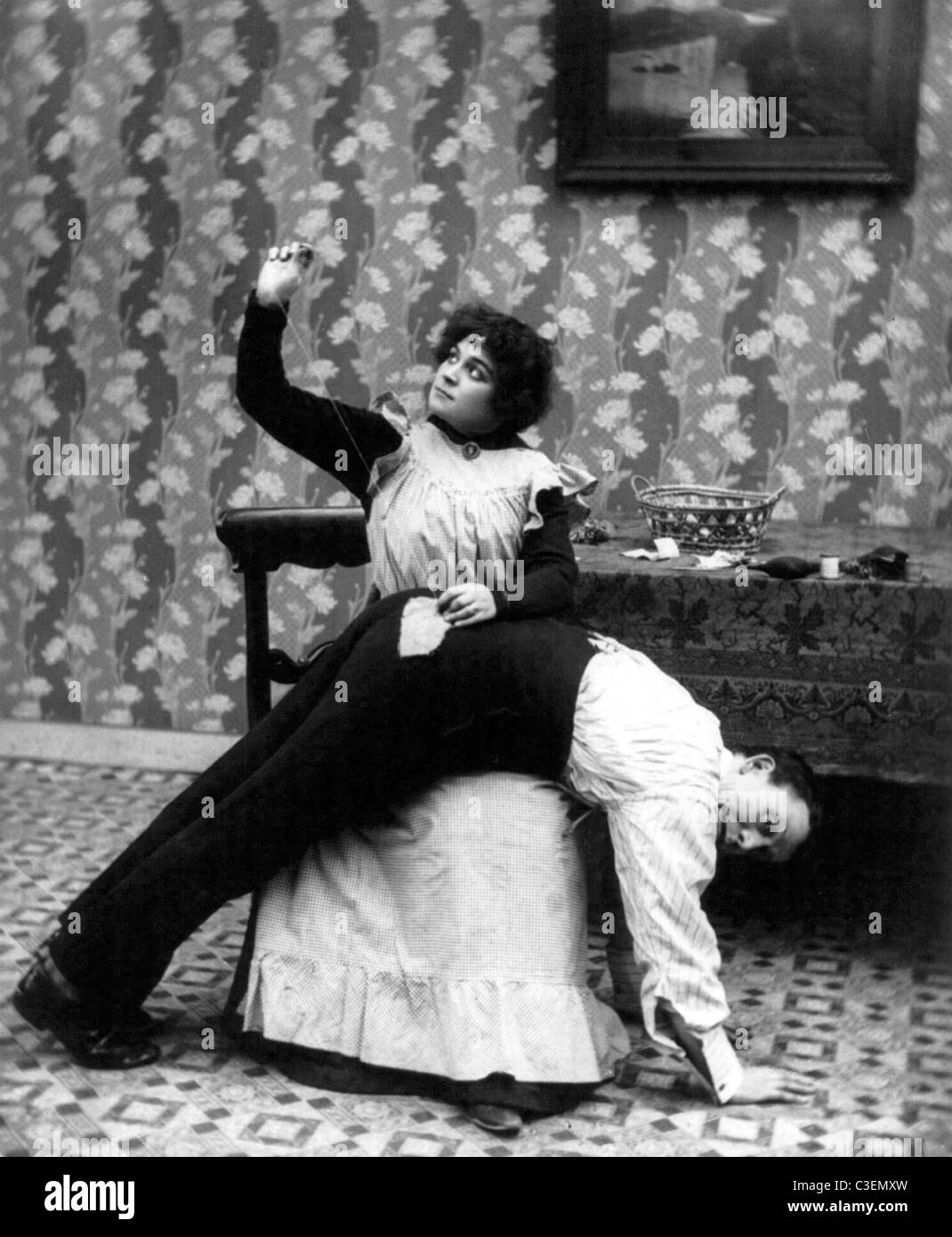 Una puntada a tiempo ahorra nueve - el hombre inclinado sobre el regazo de mujer como ella cose parche en sus pantalones" asiento, circa 1907. Foto de stock