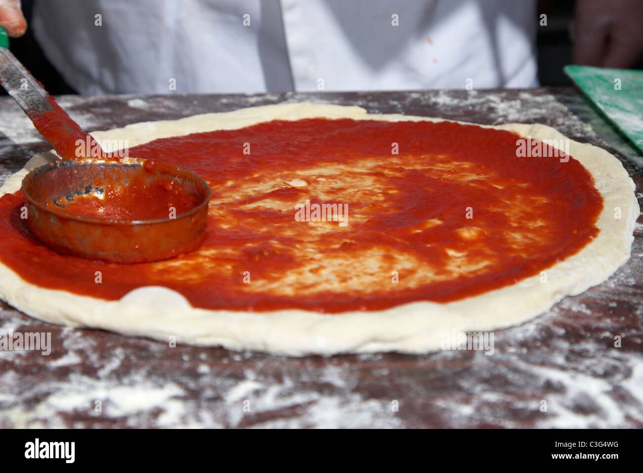 Esparcir la salsa de tomate sobre una base de masa para pizza para hacer  pizza fresca Fotografía de stock - Alamy