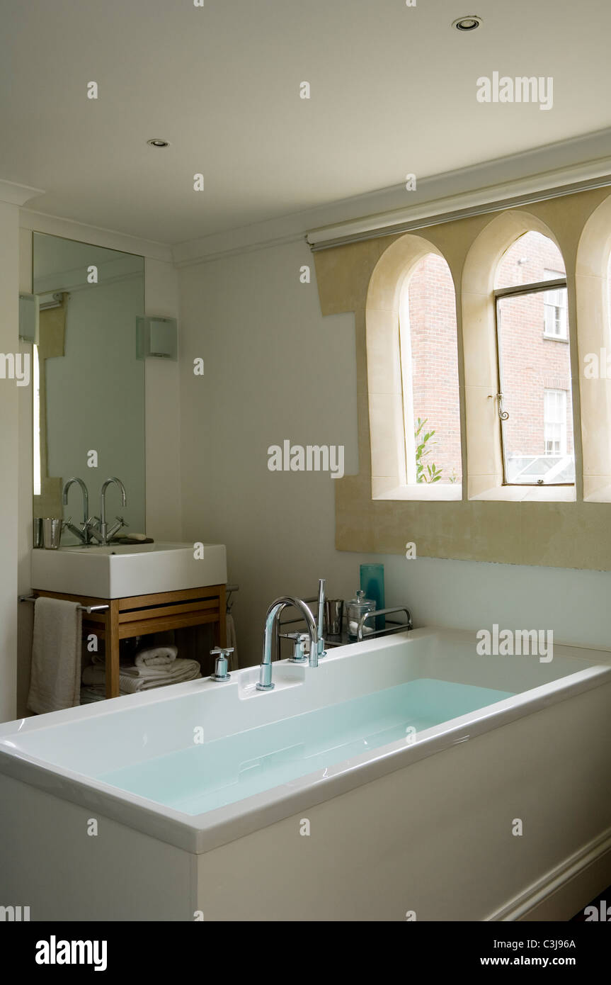 Cuarto de baño con bañera rectangular y ventanas góticas Foto de stock