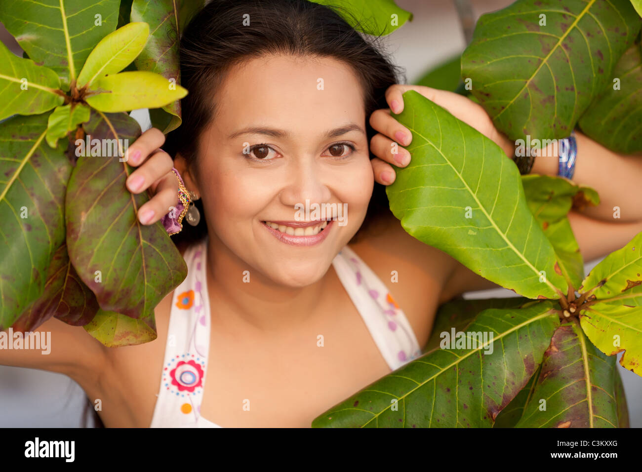 Mujer sonriente asiáticos entre grandes hojas de árbol Foto de stock