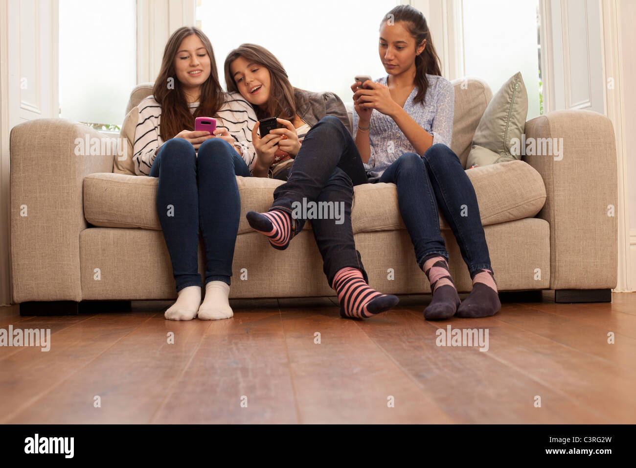 Las adolescentes sentados en el sofá mirando teléfonos Foto de stock