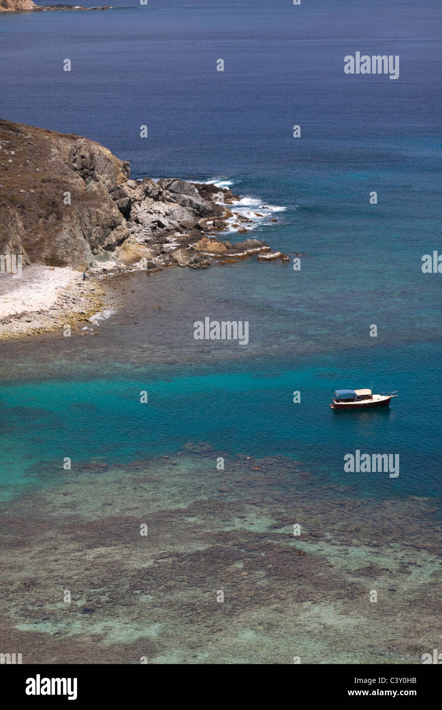 Embarcación anclada en el agua color turquesa con arrecifes de coral cerca de la orilla rocosa off Norman Island en Islas Vírgenes Británicas Foto de stock