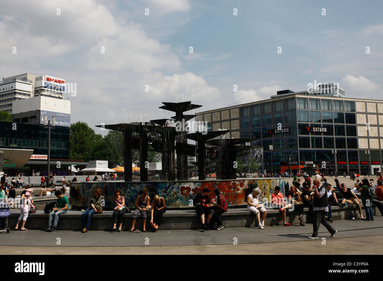 La gente se sienta alrededor de la Fuente de la 'Amistad del Pueblo' diseñada por Walter Womacka (1970) situada en la plaza pública Alexanderplatz en el distrito central de Mitte de Berlín, Alemania Foto de stock