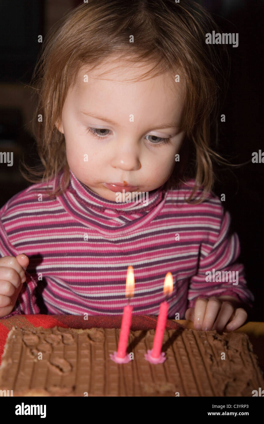 Niña de dos años mirando la tarta de cumpleaños con dos velas Foto de stock