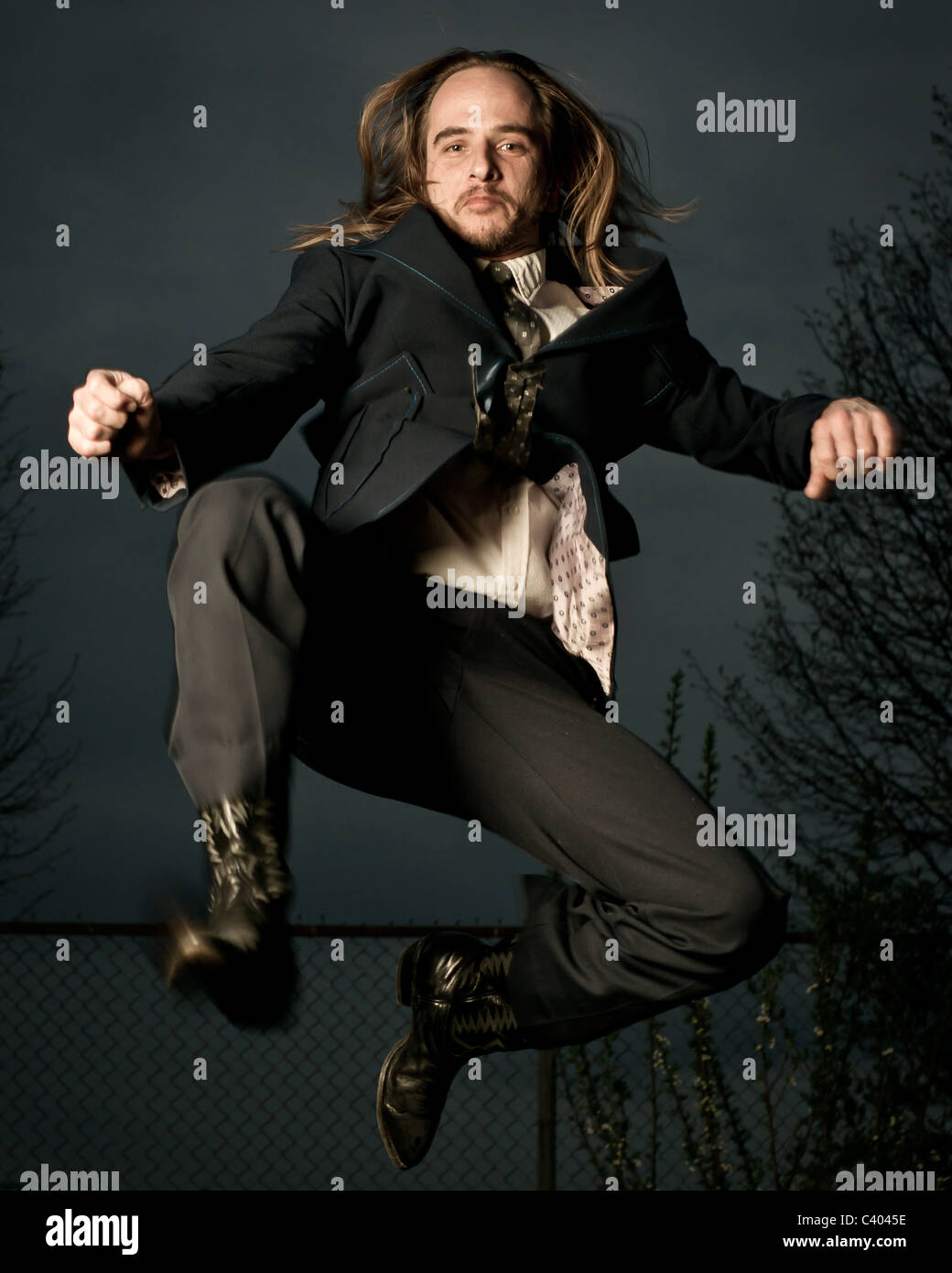 Un hombre con cabello largo en un traje de estilo retro y botas saltar en mitad del aire. Foto de stock