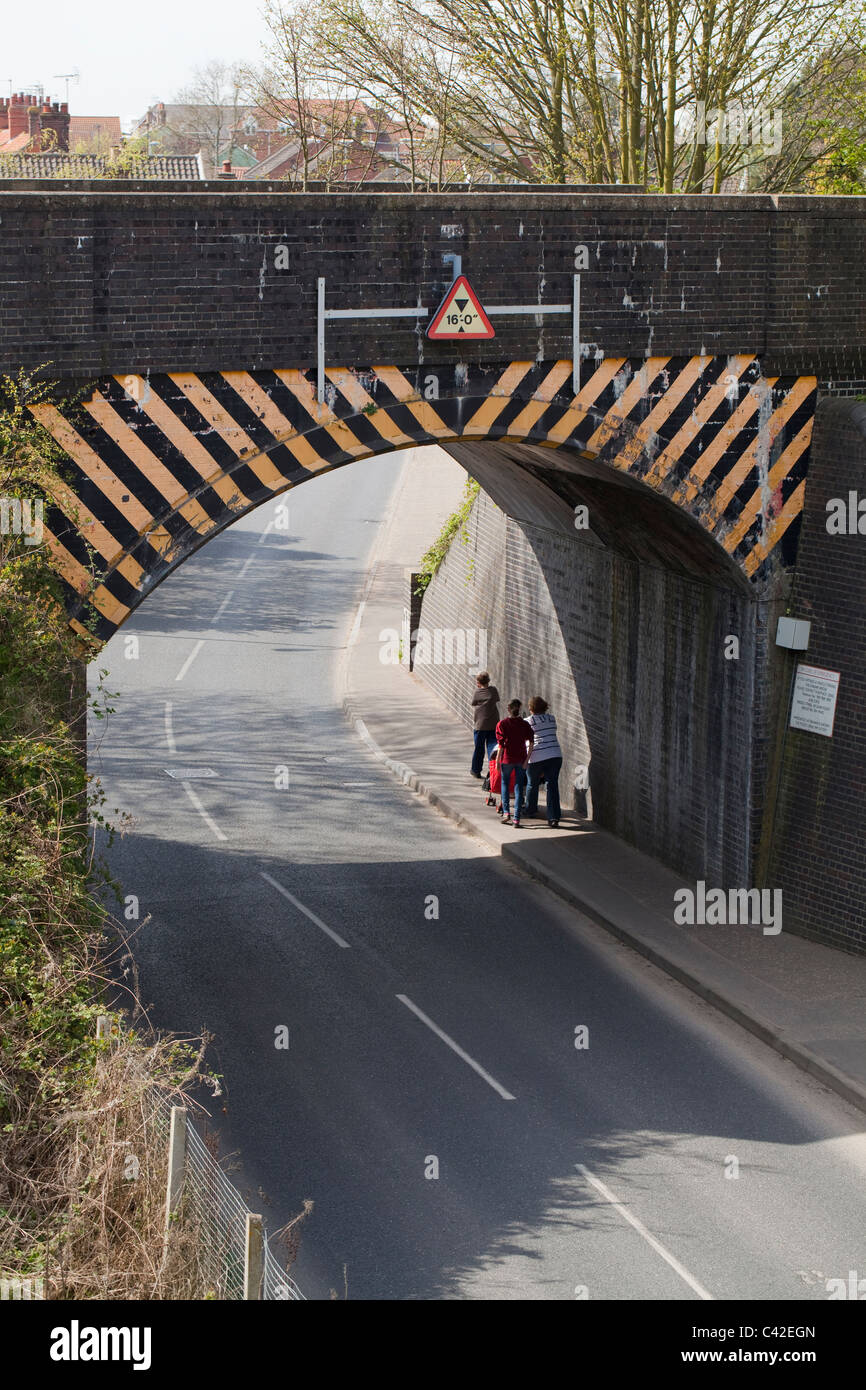 Puente ferroviario sobre una carretera. Restricción de altura en underpassing vehículos. La madre y los hijos pasando por debajo. North Walsham, Norfolk. Foto de stock