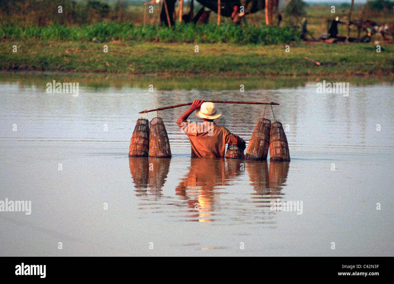 Muchacho camboyano sentar las cestas para atrapar peces del lago, distrito de Battambang, Camboya Foto de stock