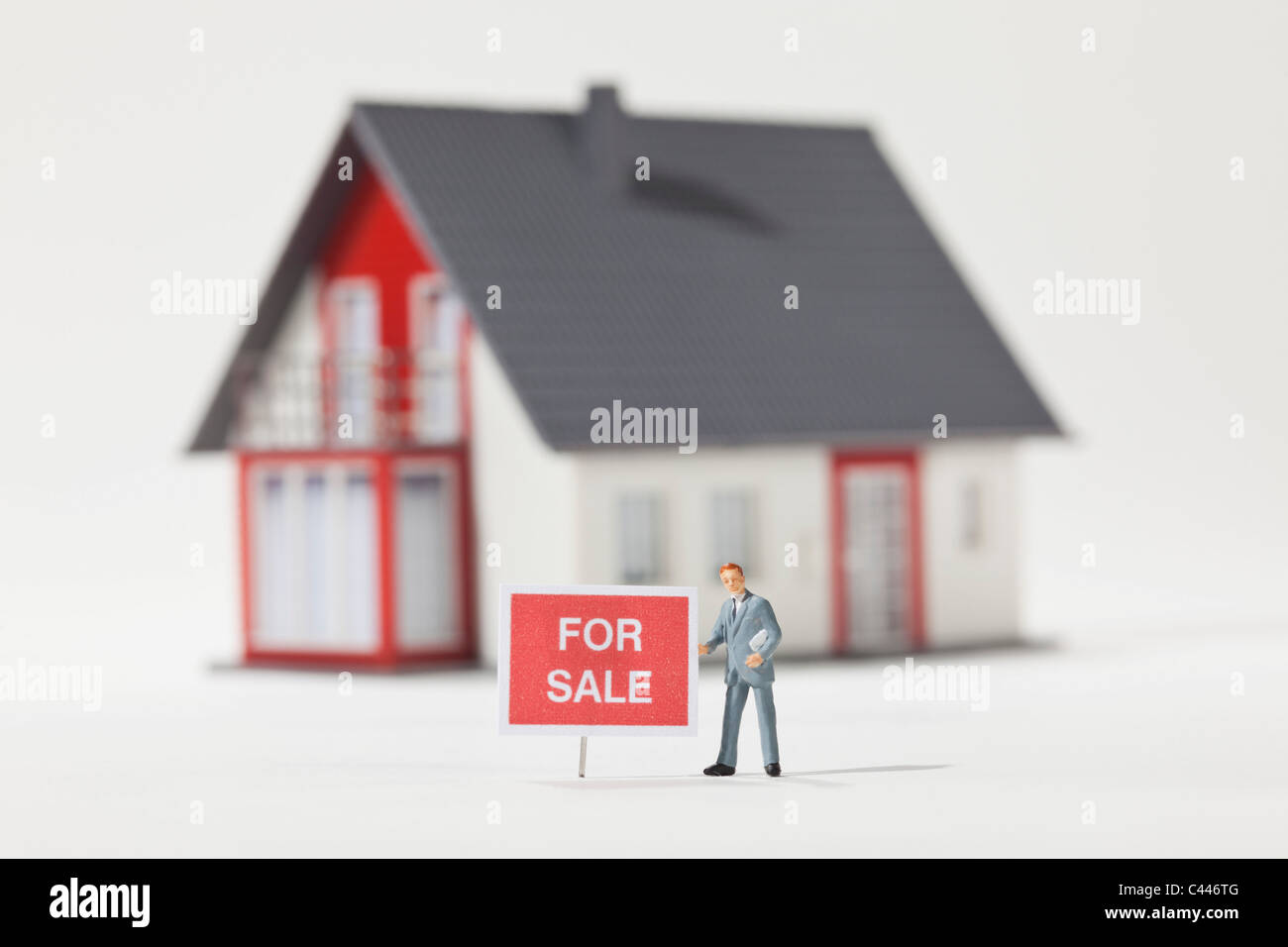 Una miniatura real estate agent figurilla de pie junto a un signo para la venta Foto de stock