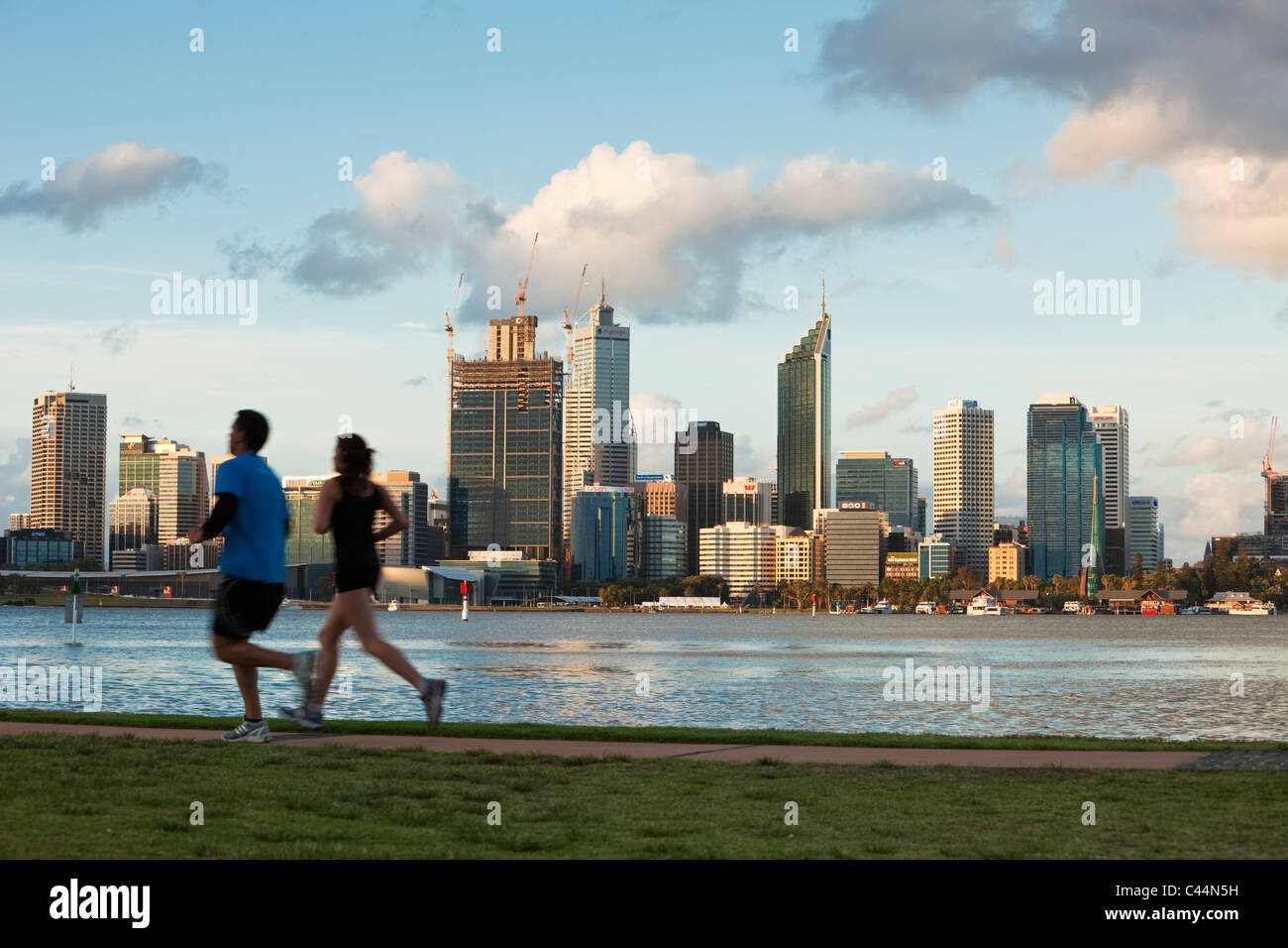 Los deportistas corriendo al lado del río Swan con vistas al horizonte de la ciudad de fondo. Perth, Australia Occidental, Australia Foto de stock