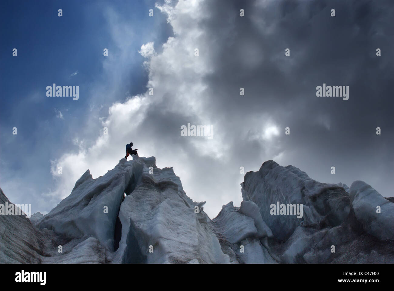 Una persona en la cima de un acantilado de hielo siluetas contra un cielo tormentoso Foto de stock