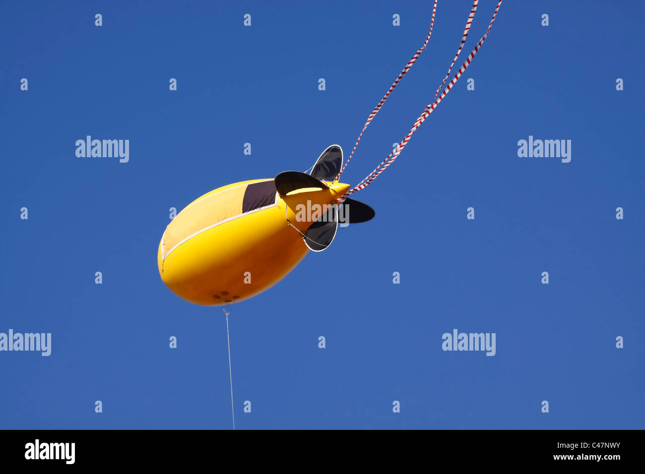Un blimp publicidad amarillo y negro o globo amarrado, aislado contra un cielo sin nubes. Foto de stock