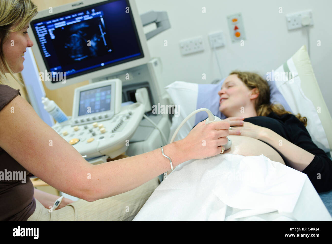 La mujer embarazada en el paciente consulta tabla con ultrasonido por la doctora Foto de stock
