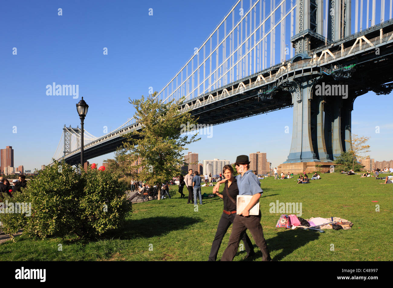 La gente en la hierba bajo el puente de Manhattan, Ciudad de Nueva York, EE.UU. Foto de stock