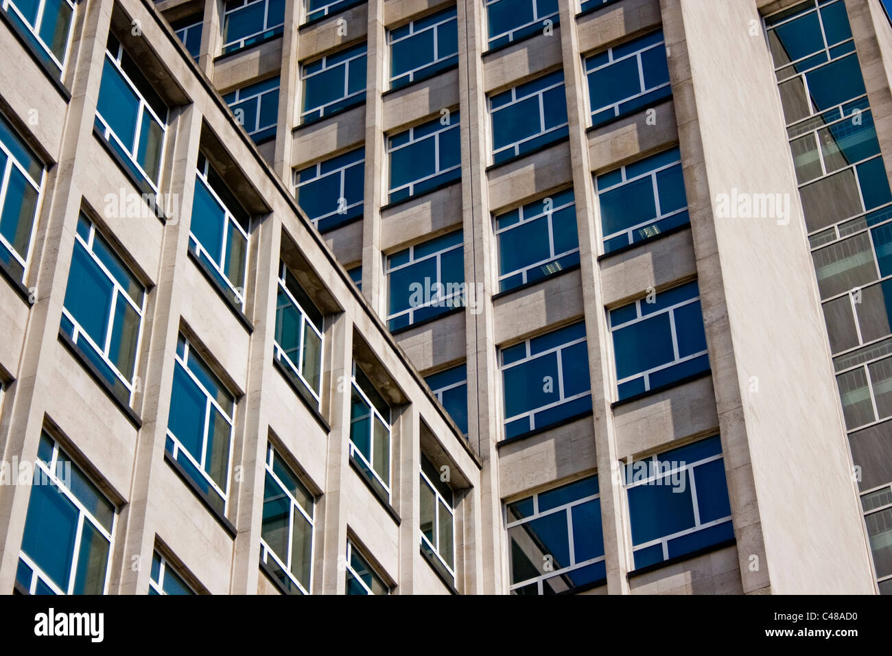 Ventanas de un bloque de oficinas concretas reflejan un cielo azul. Foto de stock