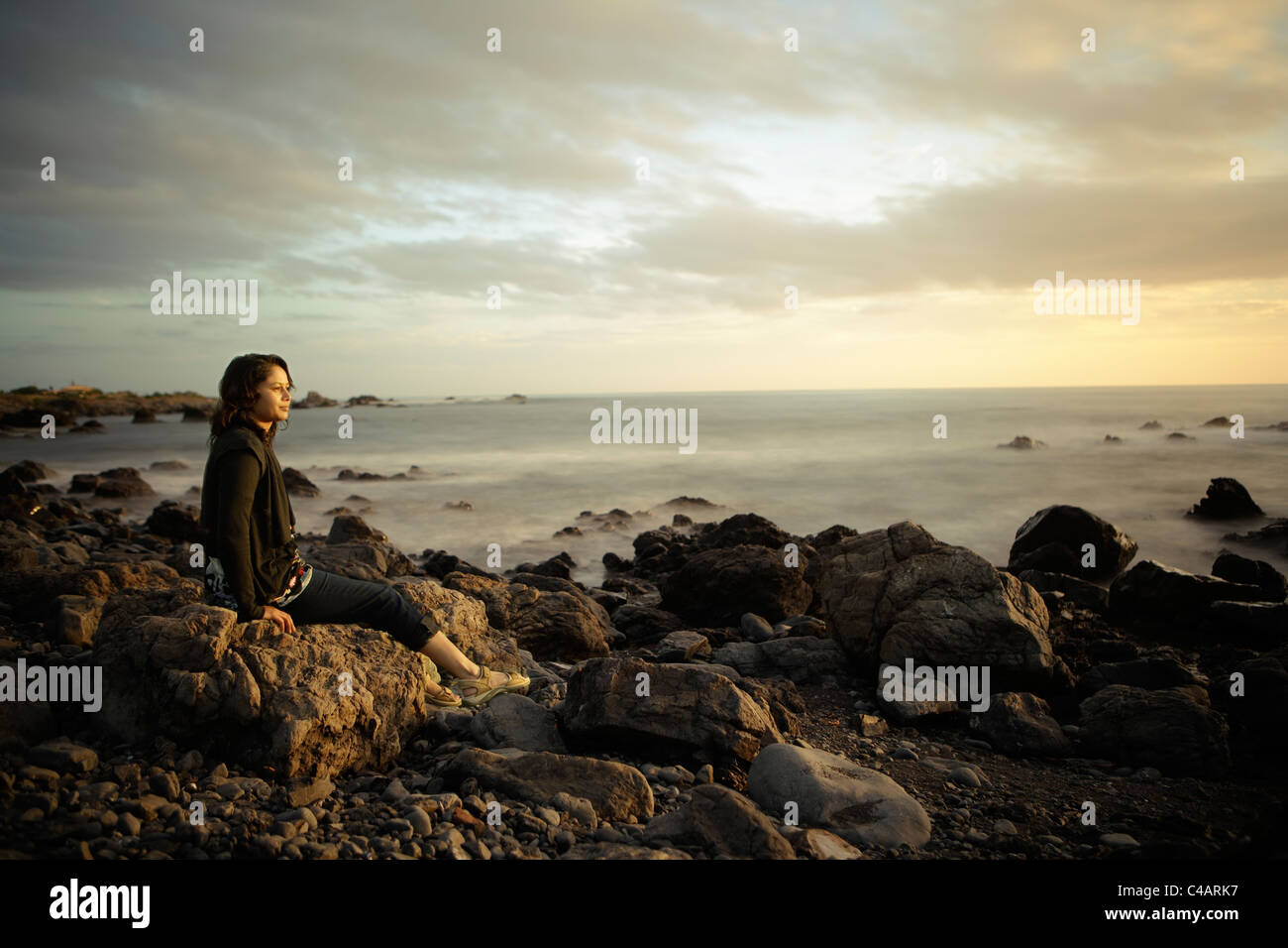 Mujer, puesta de sol, orilla rocosa, Nueva Zelanda. La exposición combinada a largo. Foto de stock