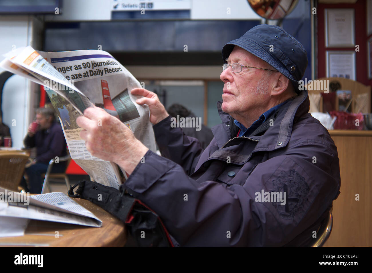 Anciano leyendo un periódico en un café en la estación de ferrocarril de la calle Queens, Glasgow, Escocia, Reino Unido Foto de stock