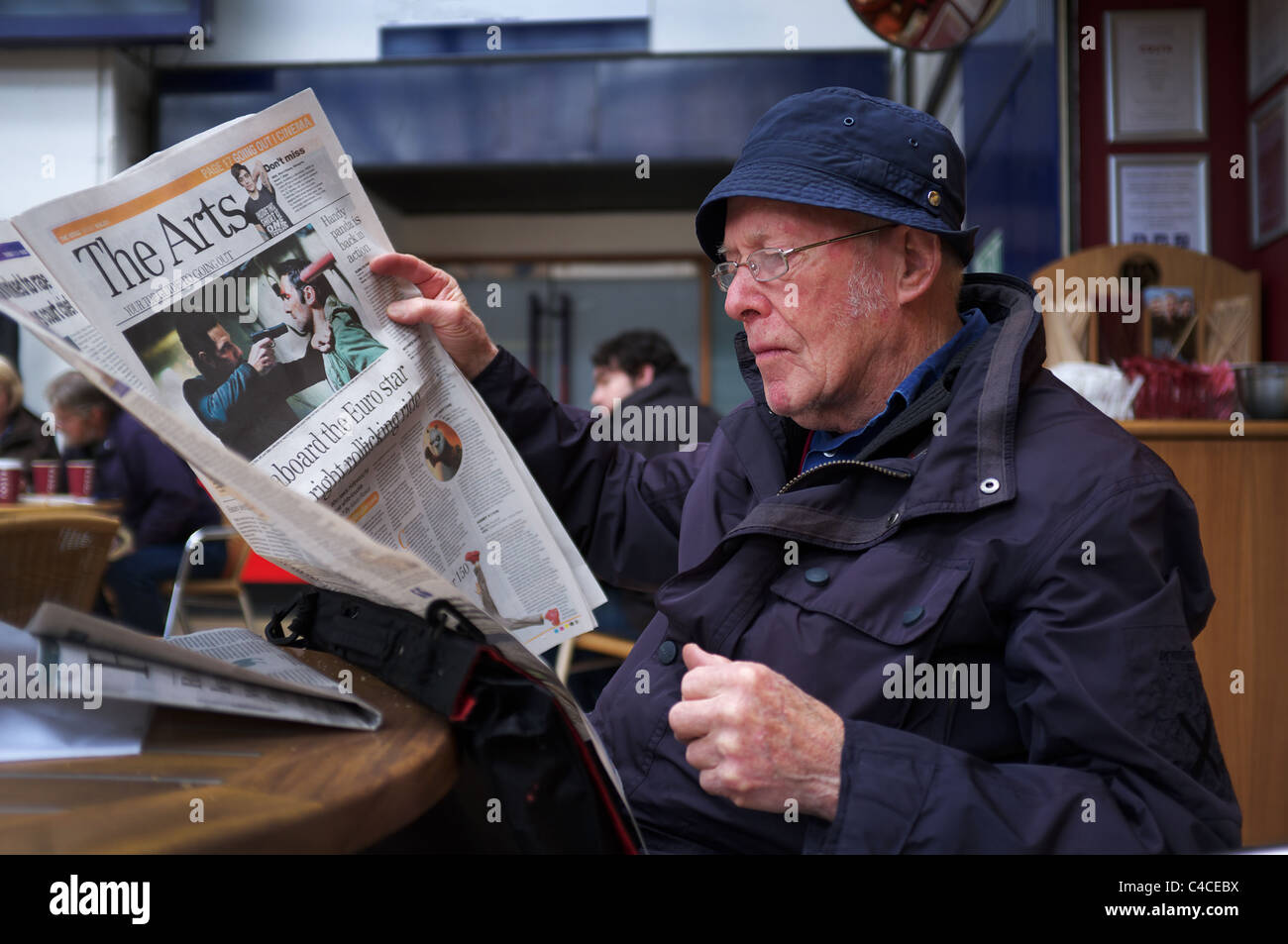 Hombre sentado en el café leyendo un periódico, estación de tren de Queen Street, Glasgow, Escocia, Reino Unido Foto de stock