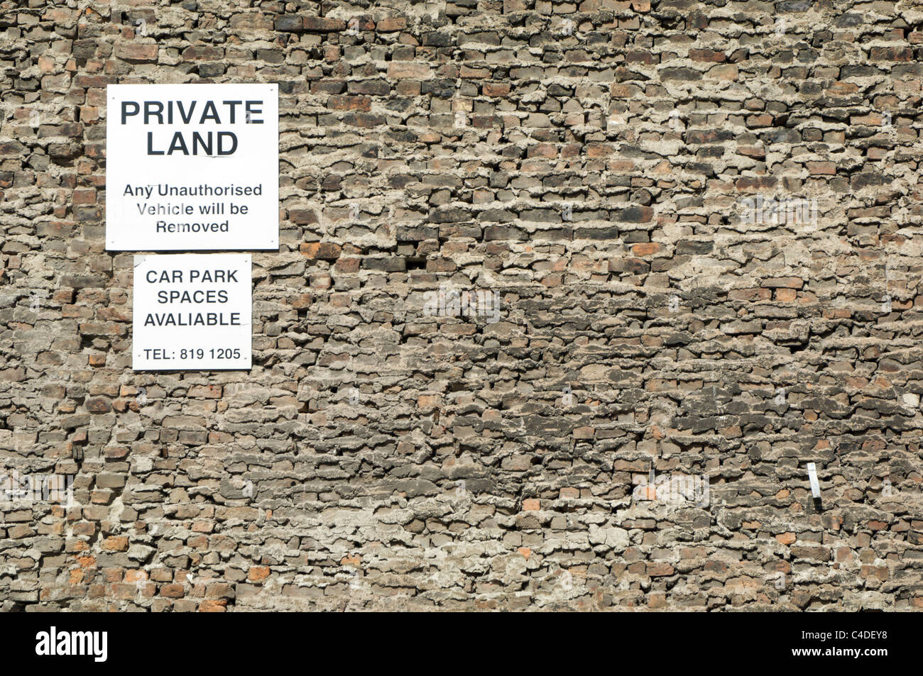 Textura de pared de ladrillos con tierra privada y aparcamiento signos, rodada en un día soleado. Punto de vista perpendicular. Foto de stock