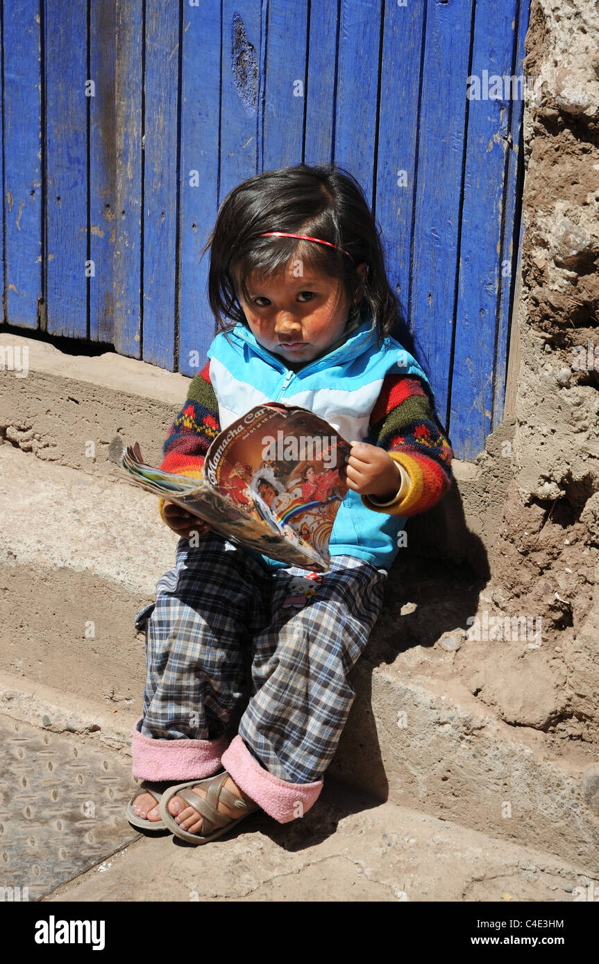Una pequeña niña peruana leyendo una revista en la calle de atrás del Cusco Foto de stock