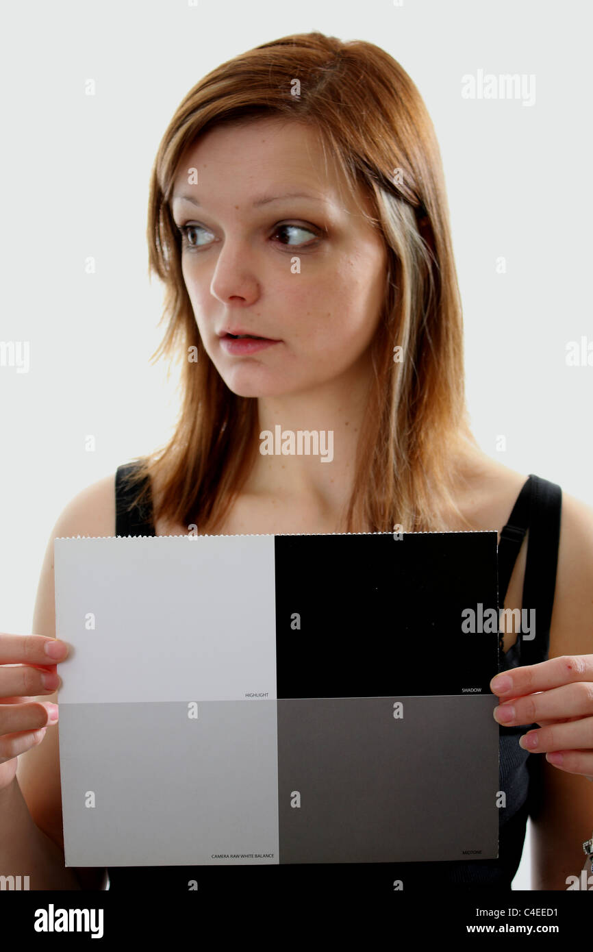 Una joven mujer sosteniendo un fotógrafos tarjeta de balance de blancos, así que él puede tomar una fotografía para ajustar el balance de blancos de la cámara. Foto de stock