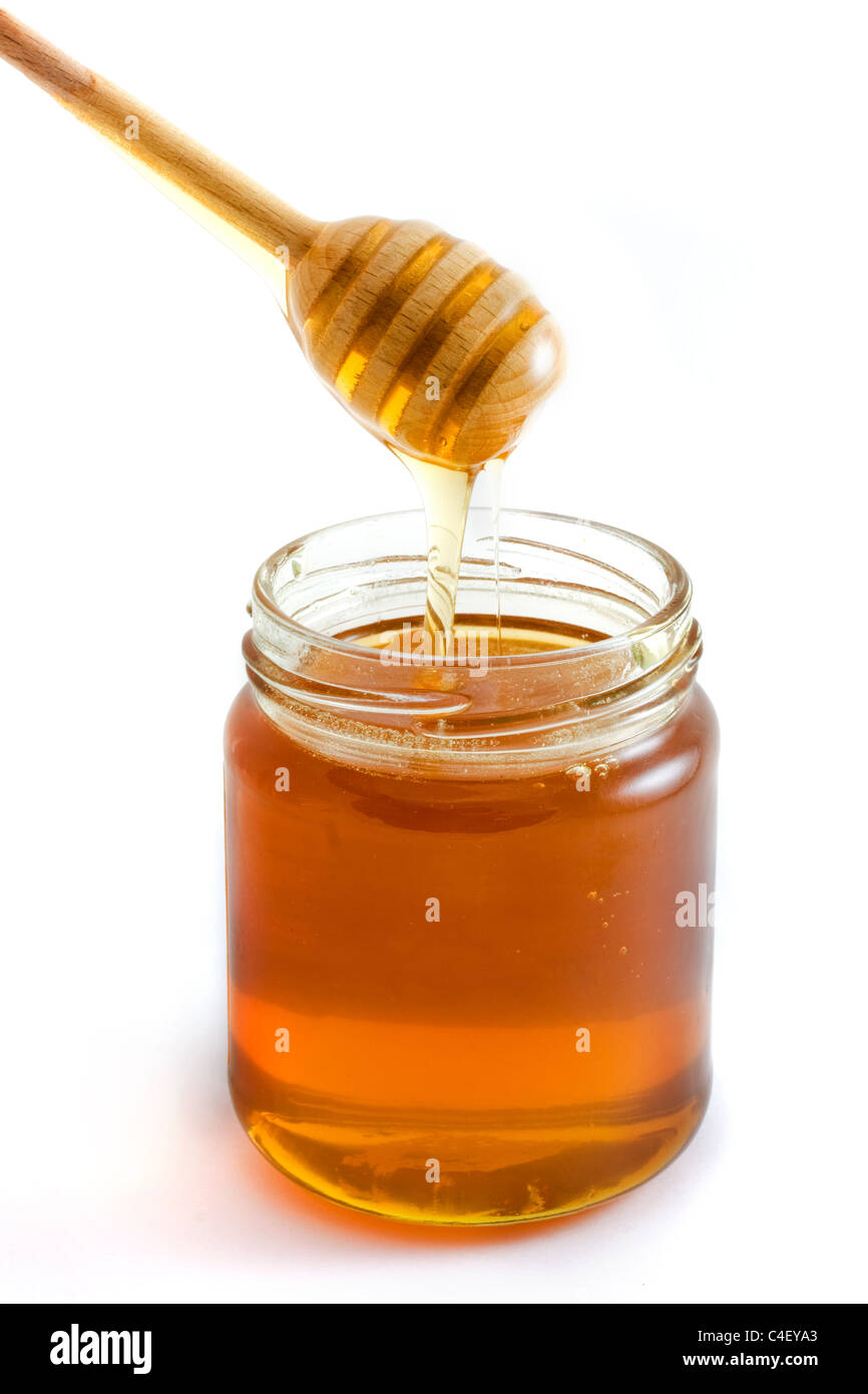Goteo de miel en el frasco aislado sobre blanco Foto de stock
