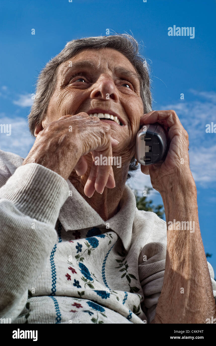 Un anciano, ciudadano senior femenino chats sobre un moderno, teléfono inalámbrico en un día soleado. Foto de stock