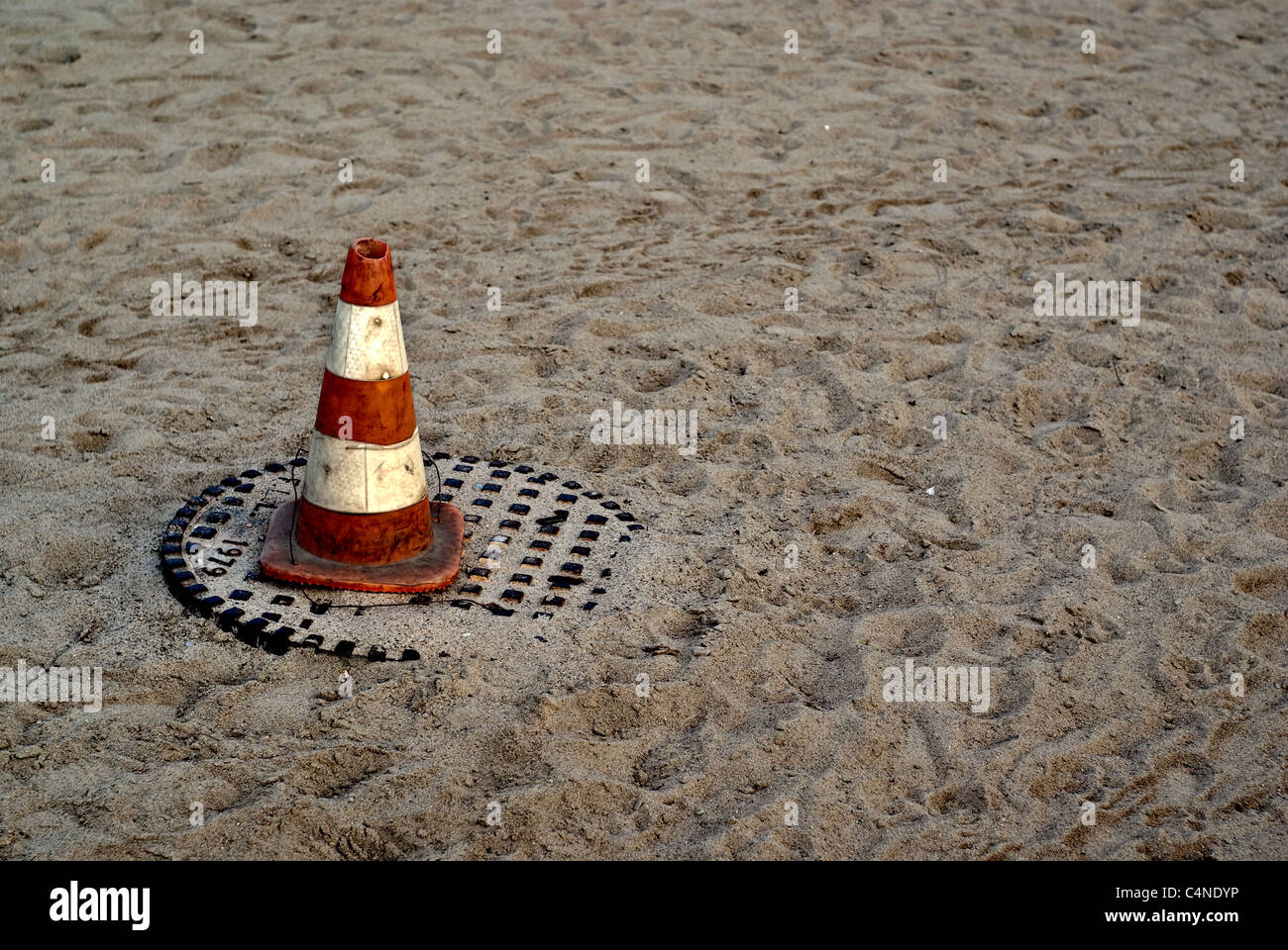 Una de color naranja y blanco pilón sentado sobre una cubierta de boca de alcantarilla en una playa de arena. Foto de stock